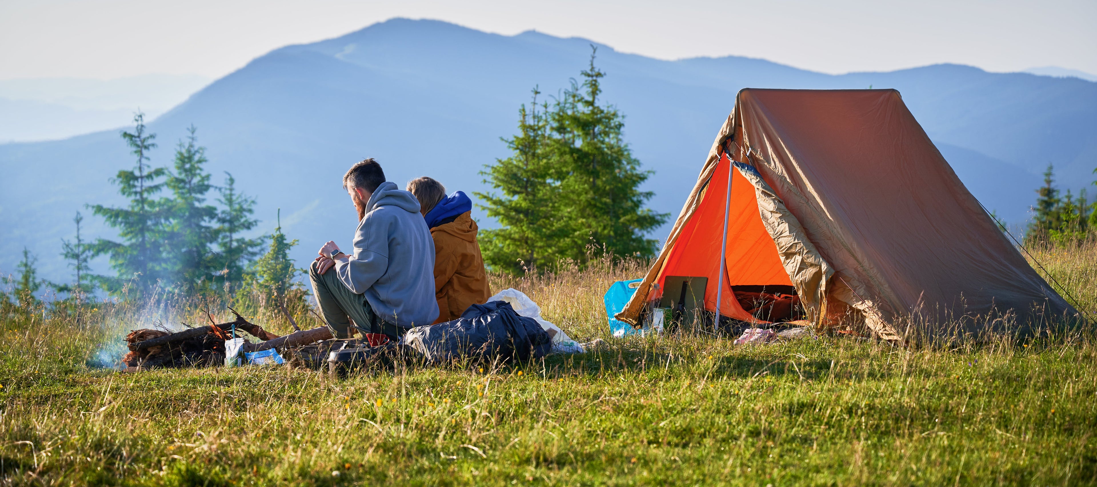 Two people sitting in front of a tent with mountains in the background
